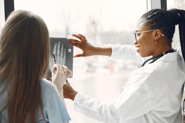 Two clinicians in white coats holding an X-ray film up to a bright window.